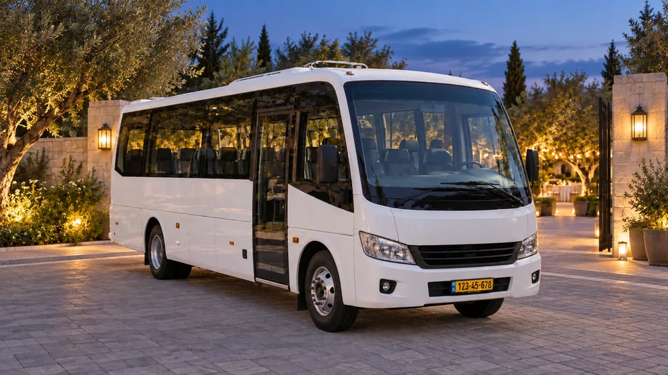 מיניבוס לבן במפרץ מרוצף ליד כניסה מוארת לגן עם עצים, בשעת ערב.