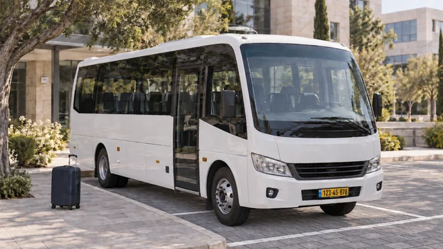 מיניבוס לבן לצד מדרכה שעליה מזוודה כחולה כהה.