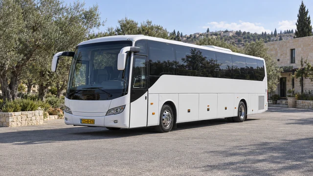 אוטובוס תיירים לבן ברחבת אספלט לצד עצי זית ומבנה אבן.